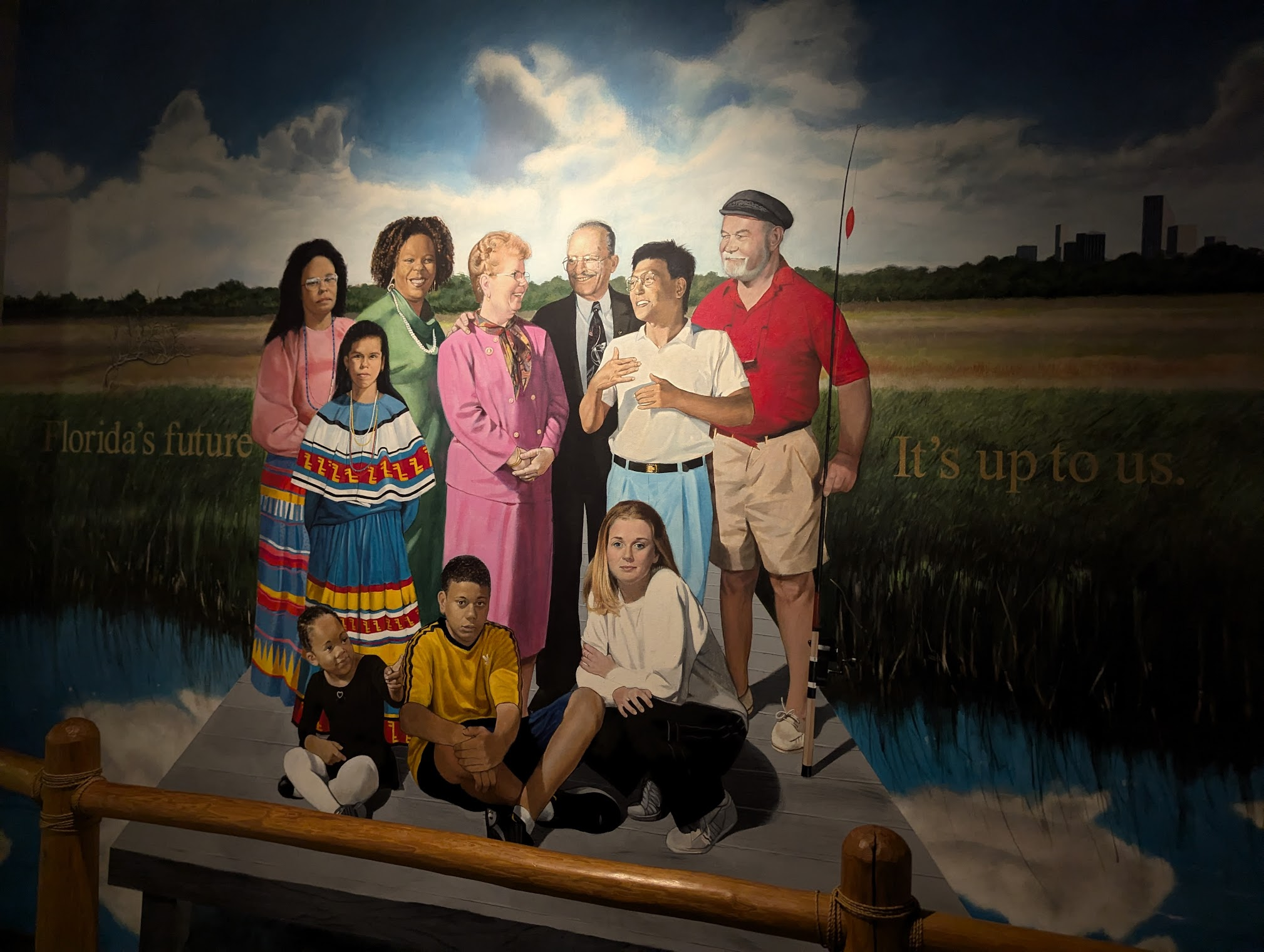image GenAI Alt text: Painting of diverse group of people standing and sitting on a dock in a natural landscape with cloudy sky and skyline in the distance, text saying Florida's future It's up to us